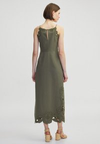 Sukienka z lnu w oliwkowym kolorze, z dopasowanym gorsetem, delikatnym haftem kwiatowym u dołu i wycięciem w kształcie łezki na plecach. Swobodna długość maxi.