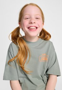 Grön bomull t-shirt med korta ärmar, med en orange grafisk tryck. T-shirten har en avslappnad passform och en mjuk textur.