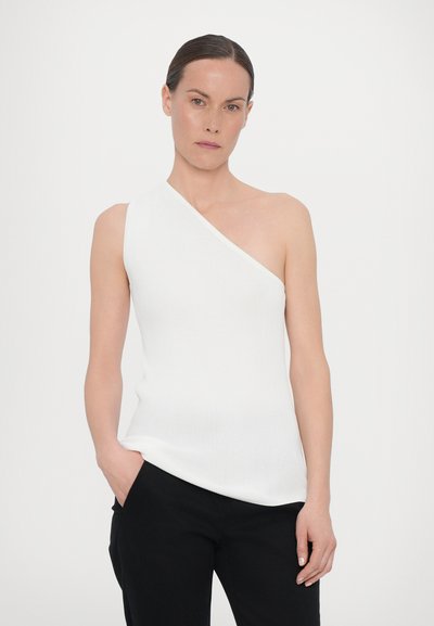 Λευκό, ριγωτό αμάνικο τοπ με ασύμμετρο σχέδιο στους ώμους. Φοριέται με μαύρο παντελόνι, που έχει λεία υφή και εφαρμοστή σιλουέτα.