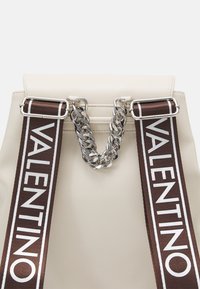 Krämfärgad läderväska med bruna tygremmar som har "Valentino" i vitt, kopplade med en kraftig silverkedja.