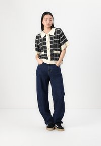 Black and white checked short-sleeve cardigan with a cream collar and buttons, paired with loose blue denim pants and black sneakers.