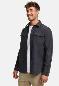 Dark gray button-up shirt made of wool blend, featuring two chest pockets, a notch collar, and a straight hem. Worn over a white T-shirt.
