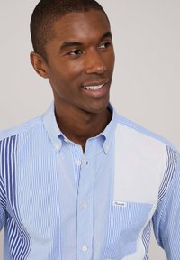 Camicia button-up con una combinazione di righe blu e bianche, in tessuto cotone, colletto standard e una tasca a toppa con dettagli di branding.