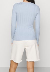 Haut à manches longues côtelé bleu clair au design ajusté, avec un col rond et une texture subtile, associé à un short en denim blanc.