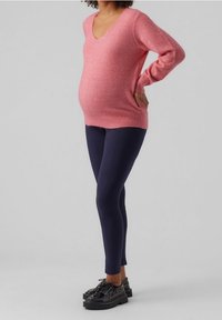 Rosa gestrickter Umstandsjacke mit V-Ausschnitt und langen Ärmeln, kombiniert mit marineblauen Leggings und schwarzen Plateauschuhen. Glatte Textur, lässiges Design.