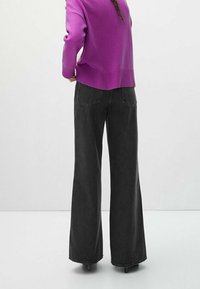 Jeans neri a gamba larga con vita alta, cuciture a contrasto e tasche posteriori, abbinati a un maglione viola. Il tessuto appare morbido.