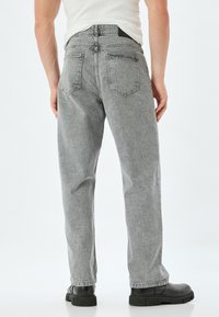 Vaqueros de mezclilla gris con corte recto, diseño de cinco bolsillos, textura desgastada y detalles de costura visibles. Llevados con botas negras.