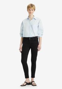 Camisa de botones a rayas azul claro, jeans ajustados negros y sandalias negras de tiras. Tejido suave, cuello estándar y detalles mínimos.