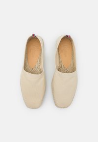 Espadrilles en toile beige avec semelles en jute tissé. Talons arrondis et panneaux élastiques sur les côtés. Accent rouge, blanc et bleu sur le talon.
