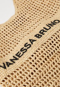 Geantă din paie țesută, cu o textură deschisă, asemănătoare cu o plasă. Are un logo brodat negru „VANESSA BRUNO” pe o bandă solidă. Culoare bej neutră.