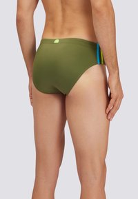 Olivgrüne Schwimmslips mit glatter Textur, die an den Seiten blaue und gelbe Streifen sowie ein grünes Logotag auf der Rückseite haben.