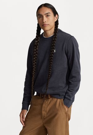 Sweatshirt bleu marine avec col rond et poignets côtelés, associé à un pantalon marron. Comprend un petit logo brodé sur la poitrine.