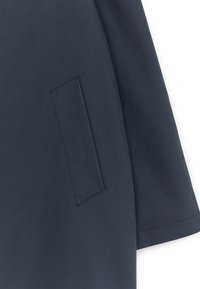 Mørkeblå kåreærme og sidelomme med ren syning på glat stof mod en hvid baggrund.