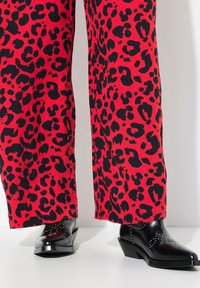Rode broek met luipaardprint en wijde pijpen, met een zwarte, glanzende afwerking aan de zoom, gecombineerd met zwarte, gestifte enkellaarsjes.
