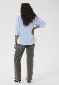 Chemise texturée bleu clair avec des manches bouffantes, associée à un pantalon droit gris et des talons ouverts noirs, présentant un look décontracté.