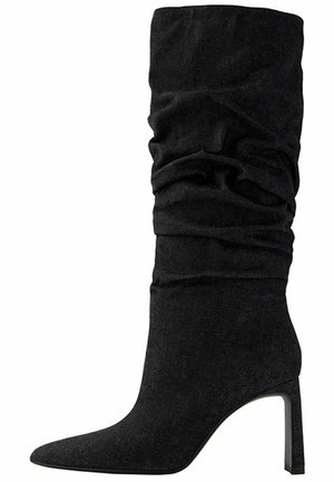 Czarny zamszowy but za kostkę o luźnym kroju, z ostrym noskiem i wąskim wysokim obcasem.