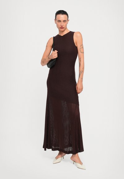 Knit, sleeveless dress in dark brown, featuring a fit-and-flare silhouette, ribbed texture, and sheer bottom panel. Paired with a small black bag.