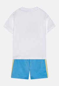 T-shirt bianca in cotone con maniche corte, abbinata a pantaloni corti blu con strisce laterali gialle. Tessuto morbido, vestibilità casual.