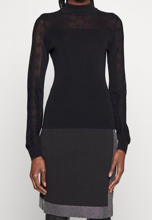 Czarny dopasowany top z długim rękawem z przezroczystą koronkową częścią rękawów i karczkiem, zestawiony z czarną spódnicą z srebrnym obszyciem w formie ćwieków.