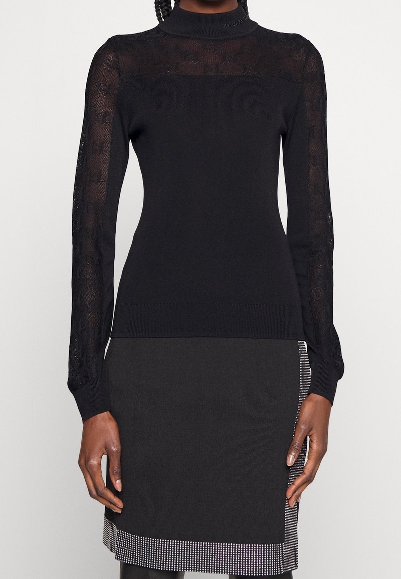 Haut noir ajusté à manches longues avec manches et empiècement en dentelle transparente, associé à une jupe noire avec un ourlet orné de clous argentés.