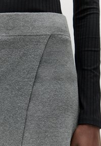 Grijze gebreide rok met een brede tailleband, met een gladde textuur en een asymmetrisch ontwerp. In combinatie met een zwart ribbel langarmtop.