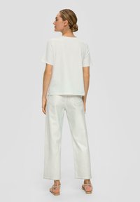 Haut blanc à manches courtes avec une coupe droite, associé à un jean à jambes larges de couleur claire. La tenue présente un design simple et une texture douce.
