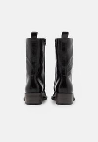 Botines de cuero negro con acabado suave, caña recta, cremallera trasera y tacones de madera apilados. Sin patrones ni adornos visibles.