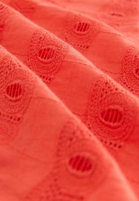 Tissu rouge avec des motifs en dentelle circulaires en relief et des lignes diagonales cousues créant de la texture et de la profondeur sur la surface.
