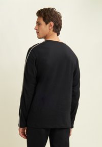 Maglietta nera a maniche lunghe con colletto a girocollo, caratterizzata da strisce bianche a contrasto sulle spalle. Realizzata in tessuto liscio e leggero.