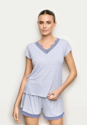 Kobieta ubrana w jasnoniebiesko-biały pasiaste krótkie rękawy i spodenki piżamowe z niebieską koronkową lamówką, stojąca na jednolitym tle.