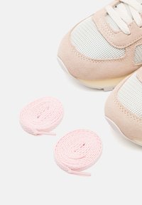 Sneaker in camoscio pesca e grigio con dettagli in mesh, lacci bianchi e lacci rotondi rosa esposti a fianco.