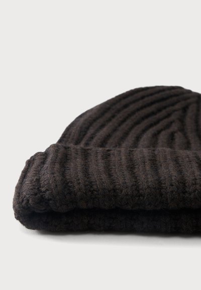 Bonnet en maille côtelée marron foncé plié sur un fond gris clair.