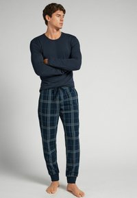 Marineblauwe longsleeve top met een ronde hals, gecombineerd met geruite pyjamabroek in donkerblauw, grijs en lichtblauwe tinten. Zachte stof, elastische tailleband.