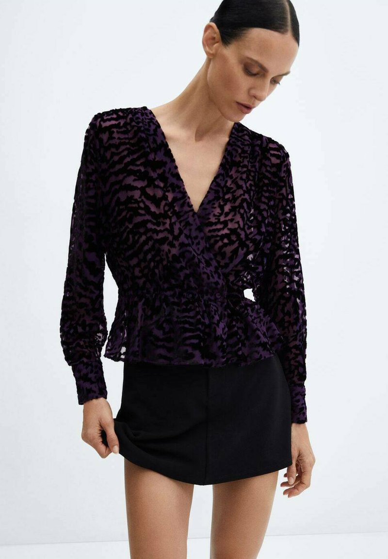 Top envolvente de manga larga transparente en color púrpura con un patrón de leopardo, que presenta un dobladillo peplum y un escote en V profundo, combinado con una falda corta negra.