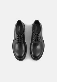 Sapatos de couro pretos com acabamento suave, bico arredondado e design de atacadores com seis pares de ilhós. Costura texturizada ao longo da sola.