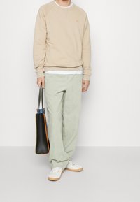 Sudadera beige con un pequeño logo naranja, pantalones anchos verde claro, zapatillas blancas y un bolso negro con detalles naranjas.