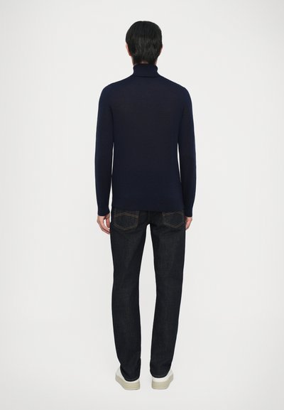 Marineblauer Rollkragenpullover kombiniert mit dunklen Jeans; der Pullover hat lange Ärmel und eine schlanke Passform, die eine glatte Wolltextur zur Geltung bringt.