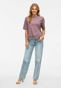 Top de manga corta en lavanda con borde de encaje en el dobladillo, combinado con jeans de pierna recta de lavado claro y sandalias de tiras beige.