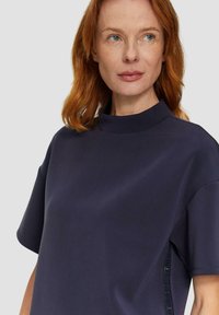 Navyblaues kurzärmliges Oberteil mit hohem Kragen, das eine glatte Textur und seitliche Akzente aus einem kontrastierenden Material aufweist.