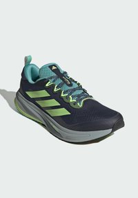 Scarpa da corsa blu navy e verde con tomaia in rete, tre strisce riflettenti, lacci testurizzati, soletta imbottita e fascia di supporto sul tallone.