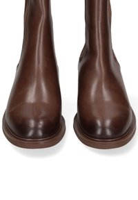 Bottes de cheville en cuir marron avec une texture lisse, bout rond et design minimaliste. Semelles en caoutchouc et sans matériel ou accents visibles.