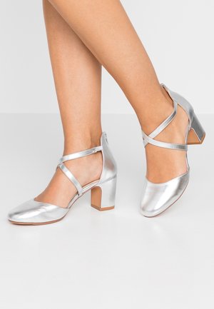 Srebrne metaliczne szpilki z kwadratowym noskiem i grubym obcasem. Posiadają krzyżujące się paski oraz gładką, błyszczącą fakturę.