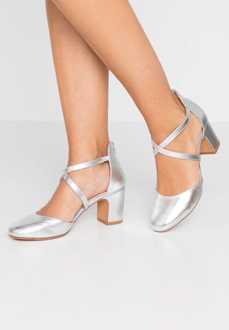 Talons métalliques argentés avec un bout carré et un talon bloc. Caractérisés par des brides croisées et une texture lisse et brillante.