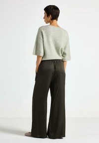 Maglione corto a maniche corte di colore grigio chiaro in materiale morbido abbinato a pantaloni larghi elastici in vita di colore verde scuro. Design semplice senza motivi visibili.