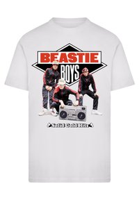 White t-shirt featuring a graphic of three figures in black and red outfits, a boombox, and the text "BEASTIE BOYS Solid Gold Hits" in bold colors.