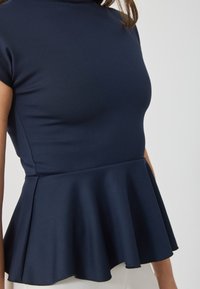 Top peplum azul marino hecho de una tela texturizada, con un cuerpo ajustado y un fondo acampanado con un borde suave, mangas cortas y cuello alto.
