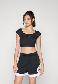 Svart kort topp med ärmar, med en logotyp på framsidan. Kombinerad med svarta shorts med vit kant och geometriskt mönster.