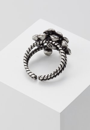 Bague ajustable en argent avec une bande torsadée et un groupe de pierres rondes facettées, foncées et claires, sur le dessus, exposée sur une surface blanche.
