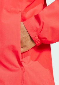 Bright coral rain jacket features a smooth, waterproof fabric, elastic cuffs, and a hidden pocket for functionality.