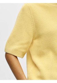 Pull jaune tricoté à manches courtes, présentant un motif texturé et une coupe décontractée. Aucun accessoire ou accent distinct n'est visible.